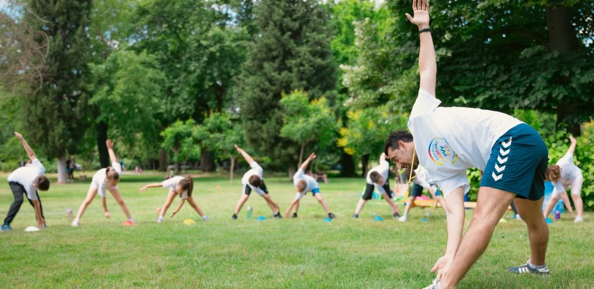 Kids stretching exercises in a park guided by a coach, promoting fitness and fun.