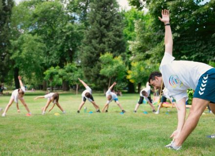 Kids stretching exercises in a park guided by a coach, promoting fitness and fun.