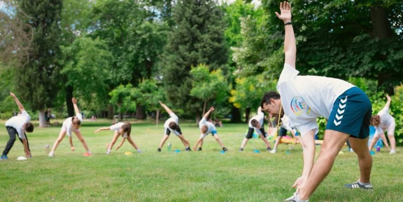 Kids stretching exercises in a park guided by a coach, promoting fitness and fun.