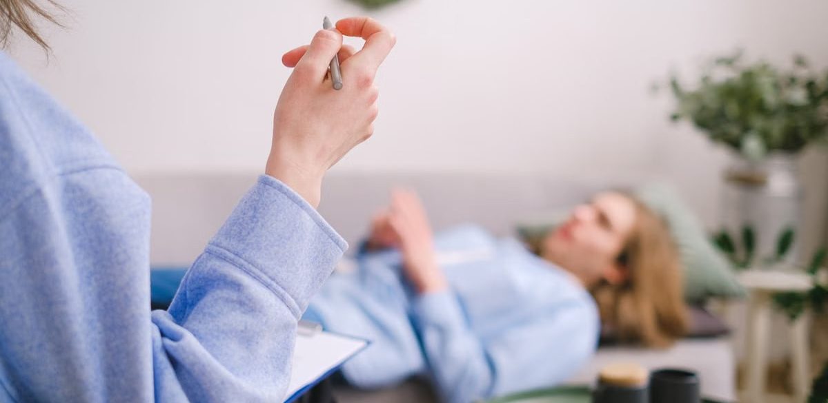 Therapist taking notes during a therapy session with a relaxed client lying on a couch.
