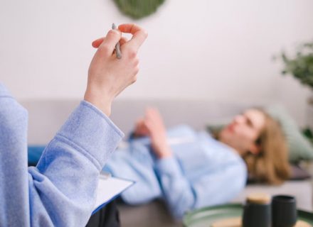 Therapist taking notes during a therapy session with a relaxed client lying on a couch.