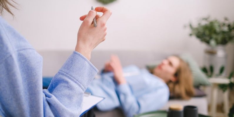 Therapist taking notes during a therapy session with a relaxed client lying on a couch.